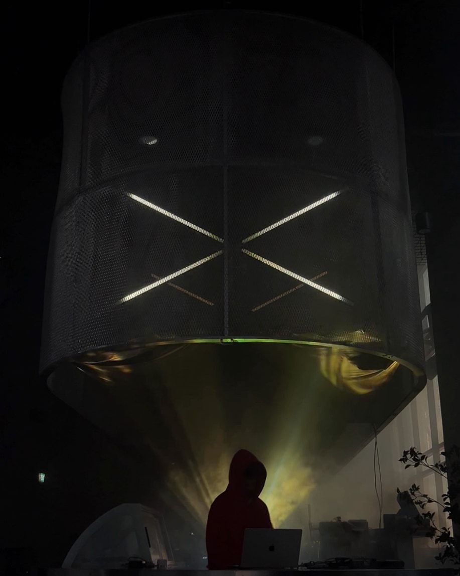 A large mesh drum hanging over a DJ booth, with white LED tubes crossing inside it.