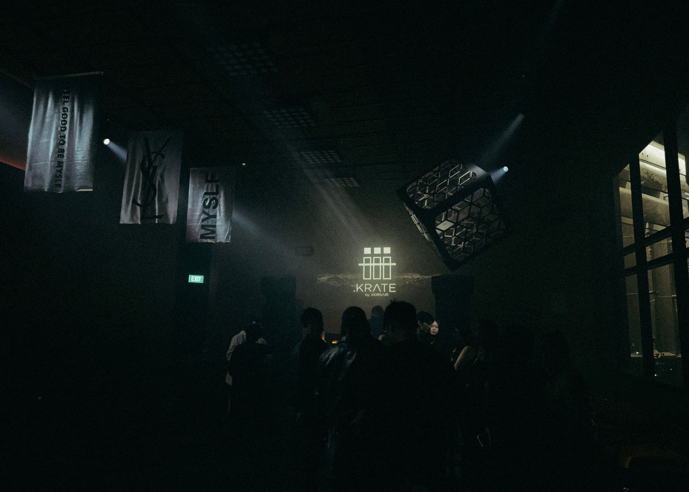 A dark room at a brand event with white beams crossing through haze above the crowd.