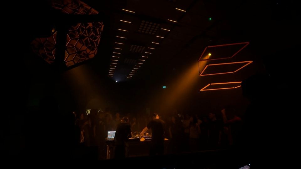 The view from behind the DJ booth, with the crowd in amber haze and a lit cube overhead.