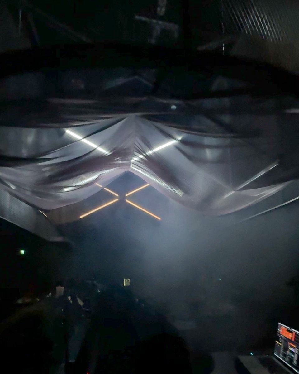 The view up from behind the DJ booth into the draped fabric, with LED tubes and haze.