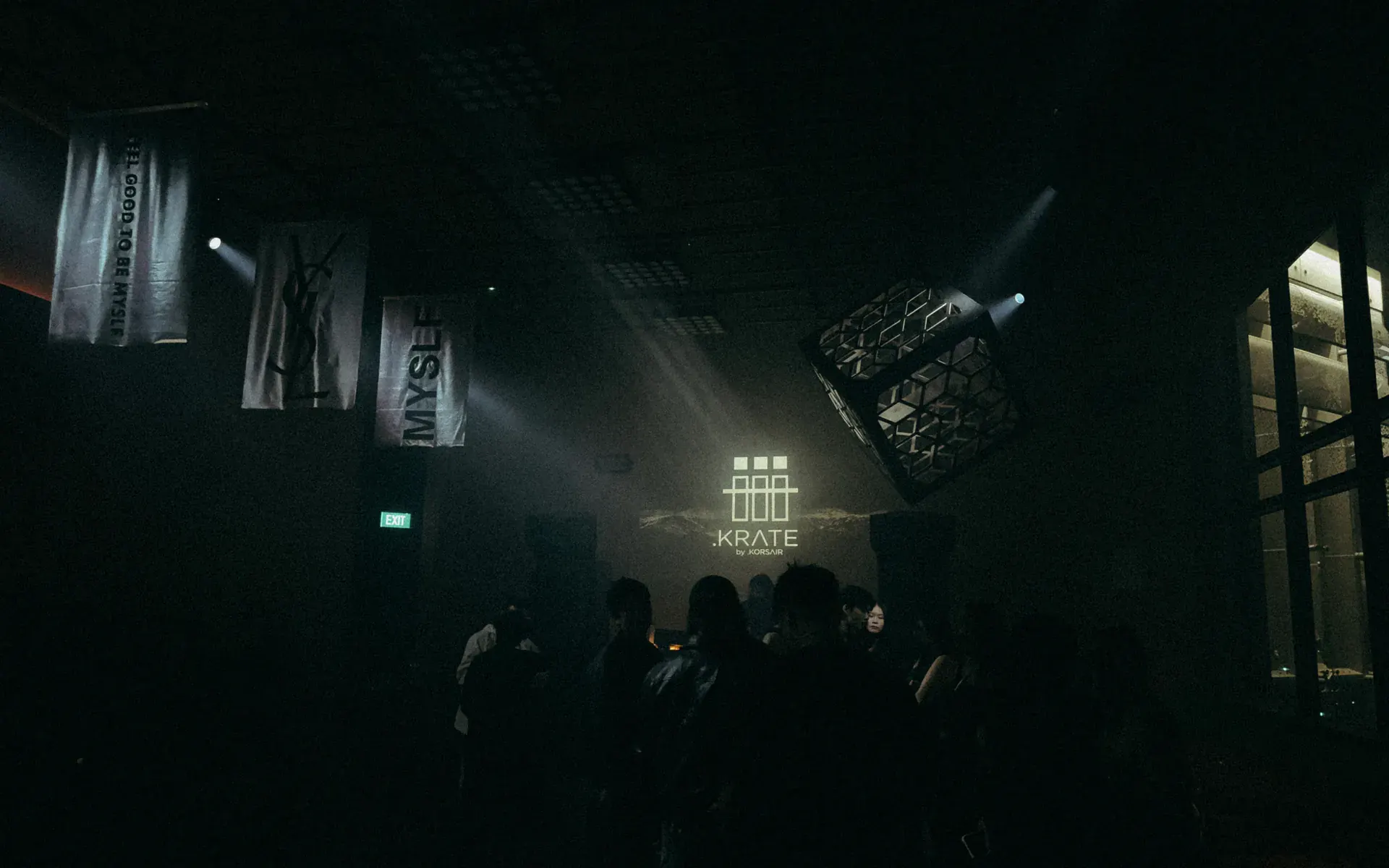 A dark room at a brand event with white beams crossing through haze above the crowd.
