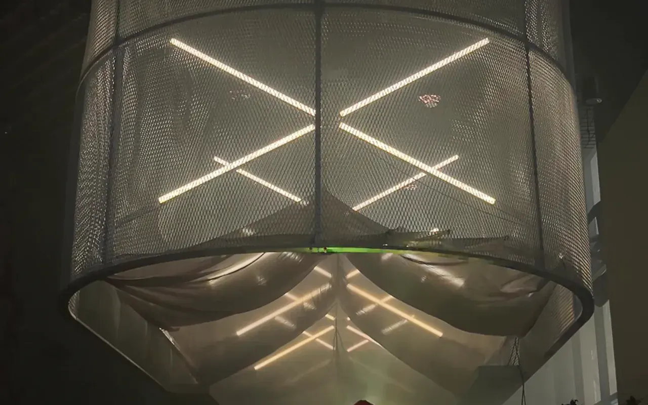 A large mesh drum hanging over a DJ booth, with white LED tubes crossing inside it.
